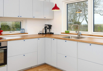 Cucina moderna con piano in legno, mobili bianchi e grandi finestre in una casa vacanze 5 stelle a Sydals, Danimarca.