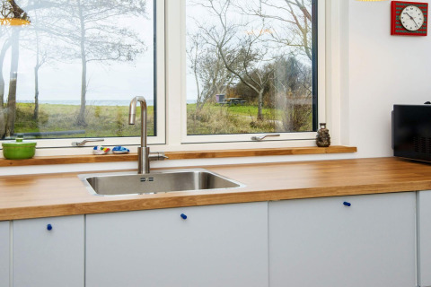Moderne gootsteen met houten aanrecht en groot raam in vijfsterren vakantiehuis in Sydals, Denemarken.