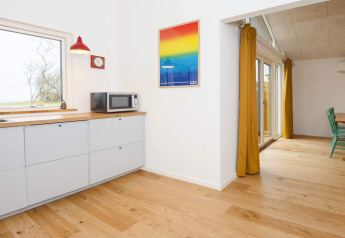 Coin cuisine lumineux dans maison de vacances 5 étoiles à Sydals, Danemark, avec sol en bois et rideaux jaunes.