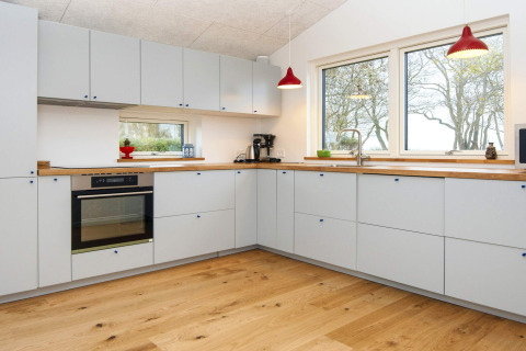 Cuisine moderne avec armoires claires, parquet et grandes fenêtres dans une maison de vacances à Sydals, Danemark.