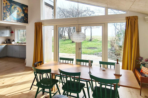 Salle à manger moderne avec chaises vertes, grandes fenêtres et vue sur jardin dans une maison à Sydals, Danemark.