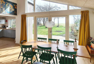 Moderne spiseplads med grønne stole, stort vindue og udsigt til haven i et feriehus i Sydals, Danmark.