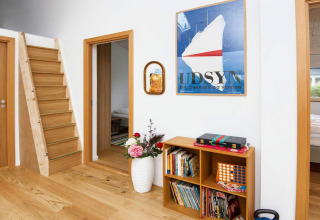 Moderne lodge in Sydals, Denemarken, met houten trap, boekenrek, kunst aan de muur en bloemenvaas.