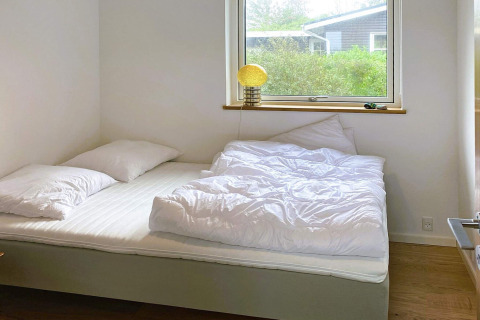 Lichte slaapkamer met dubbel bed, witte dekbedden en kussens in een 5-sterren vakantiehuis in Sydals, Denemarken.