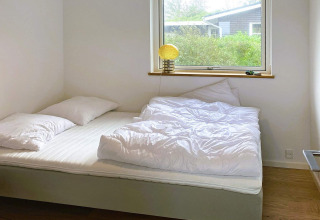Lichte slaapkamer met tweepersoonsbed, witte dekbedden en kussens in een 5-sterren vakantiehuis in Sydals, Denemarken.