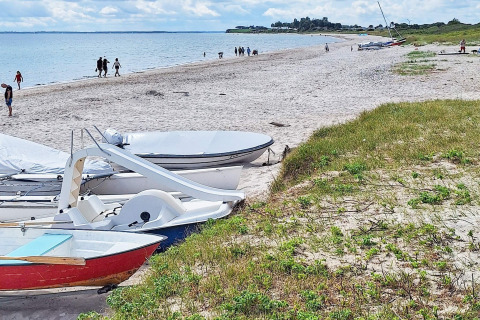 Strandbillede ved «5 stjernet feriebolig i Sydals», Danmark, med både, sand og gående mennesker.