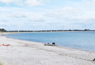 Strand mit blauem Wasser, Windräder im Hintergrund und wenigen Menschen nahe 5-Sterne-Ferienhaus in Sydals, Dänemark.