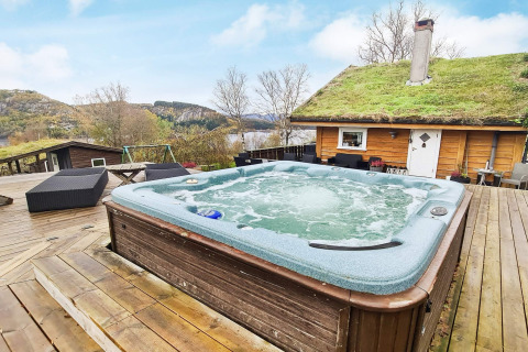 Bubbelbad buiten op houten terras bij een lodge met grasdak, omgeven door natuur in Tau, Denemarken.