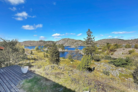 Udsigt fra HUS 55762 HYTTE A i Danmark med klar blå himmel, sø, klipper og grøn beplantning.