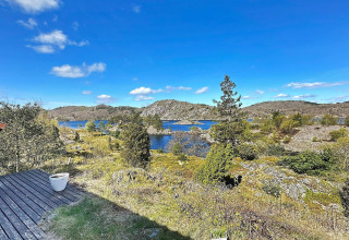 Udsigt fra HUS 55762 HYTTE A i Danmark med klar blå himmel, sø, klipper og grøn beplantning.