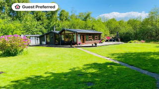 Maison de vacances pour 6 personnes à Bogense, grande pelouse verte, terrasse ensoleillée et fleurs.