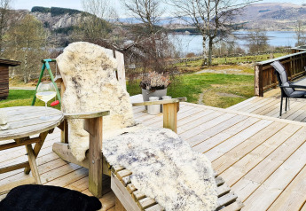 Udendørs træterrasse ved lodge i Tau, Danmark med behagelig stol, lammeskind og naturudsigt.