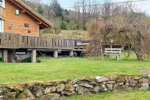 Chalet en bois avec grande terrasse, banc, balançoire et pelouse verte à la maison de vacances à Tau, Danemark.
