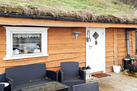 Buiten zithoek bij een houten lodge met grasdak en witte kozijnen in Tau, Denemarken.