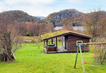 Gemütliche Holzhütte mit Grasdach, Kinderschaukel und Bergblick an einem See in Tau, Norwegen.