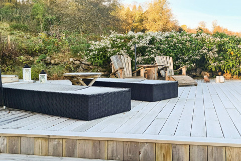 Udendørs terrasse ved 12 personers feriehus i Tau, Danmark, med loungemøbler og grøn baggrund.
