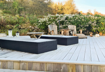 Terrazza esterna di casa vacanze per 12 persone a Tau, Danimarca, con sedie a sdraio e natura.