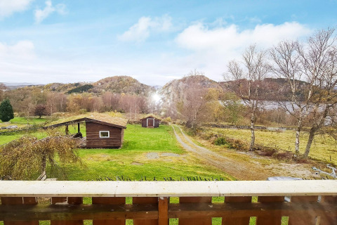 Vue d’un balcon sur des champs verts, cabanes en bois et collines au gîte 12 personnes à Tau, Danemark.