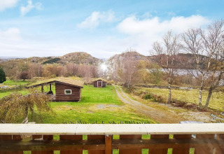 Vista desde un balcón sobre campos verdes, cabañas de madera y colinas en casa de vacaciones en Tau, Dinamarca.