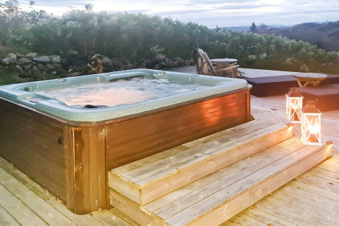 Udendørs jacuzzi med dampende vand, træterrasse og lanterner ved 12 personers feriehus i Tau, Danmark.