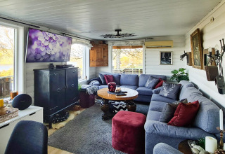 Salon chaleureux d'une maison de vacances à Tau avec grand canapé d’angle, TV et vue sur la terrasse.