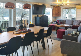 Soggiorno moderno nella casa vacanze di Tau con tavolo da pranzo, divani e grandi finestre panoramiche.