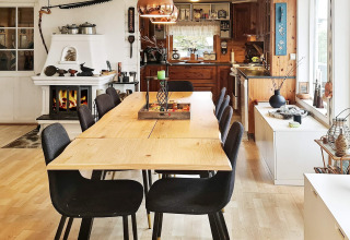Sala da pranzo con sei sedie nere, tavolo in legno, camino e cucina aperta in un lodge a Tau, Danimarca.