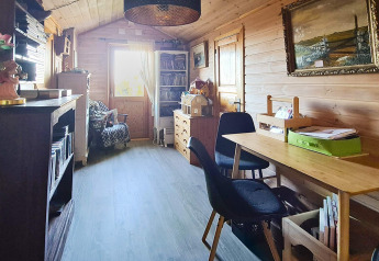 Sala con paredes de madera, escritorio, sillas negras y estanterías en casa de vacaciones en Tau, Dinamarca.