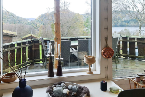 Vista dall’interno di un lodge a Tau, Danimarca, con terrazza, tavolo da pranzo e colline sullo sfondo.
