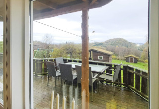 Vista desde la ventana a la terraza con mesa, sillas y cabañas en un albergue para 12 personas en Tau.