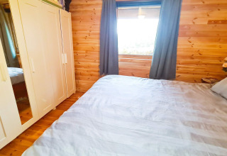 Chambre avec murs en bois, grand lit, armoire blanche et fenêtre dans « 12 person holiday home in Tau », Danemark.
