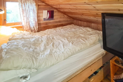Gemütliches Dachzimmer mit Doppelbett, Fernseher, Holzdecke und Tageslicht im Ferienhaus in Tau, Dänemark.