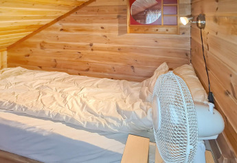 Sfeervolle houten kamer met eenpersoonsbed, wit donsdeken, ventilator en wandlamp in het Tau-huis.