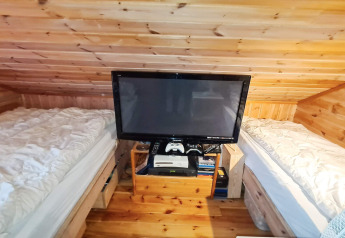 Et hyggeligt værelse med skrå træloft, to enkeltsenge og et tv mellem sengene i et feriehus i Tau.