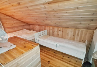 Schlafzimmer mit zwei Einzelbetten und geneigter Holzdecke in einer Ferienhütte in Tau, Dänemark.