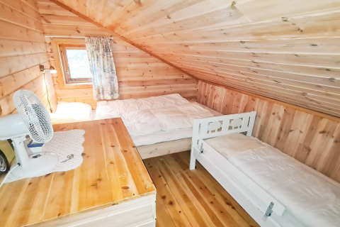 Slaapkamer met houten wanden, schuin plafond, tweepersoonsbed, eenpersoonsbed, bureau en raam in een vakantiehuis.