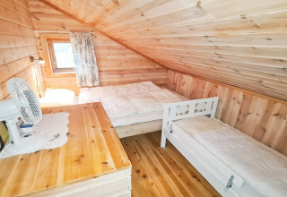 Slaapkamer met houten wanden, schuin plafond, tweepersoonsbed, eenpersoonsbed, bureau en raam in een vakantiehuis.