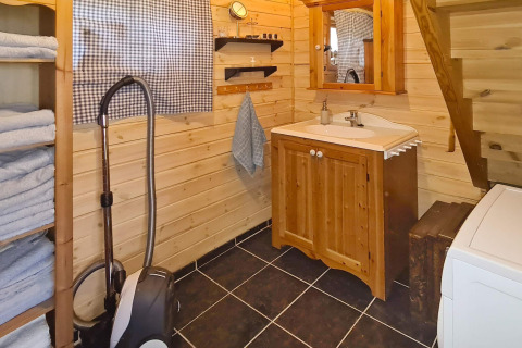 Acogedor baño de cabaña con paredes de madera, lavabo, espejo, estanterías, toallas y aspiradora.