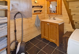 Acogedor baño de cabaña con paredes de madera, lavabo, espejo, estanterías, toallas y aspiradora.