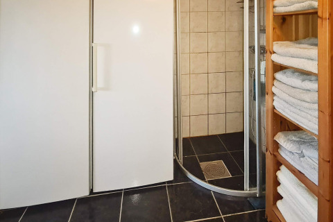 Baño de casa vacacional en Tau, Dinamarca, con ducha, armarios blancos y estantes llenos de toallas.