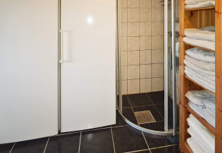 Badezimmer in einem Ferienhaus mit Dusche, weißen Schränken und Handtuchregal in Tau, Dänemark.