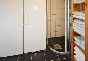 Badkamer in vakantiehuis in Tau, Denemarken met douchecabine, witte kasten en handdoekenrek.