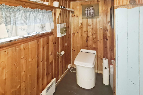 Bagno con pannelli in legno, wc moderno, mensola con decorazioni e finestra con tendine a quadri.