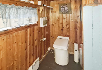 Badkamer met houten wanden, modern toilet, plank met decoratie en raam met geruite gordijnen.
