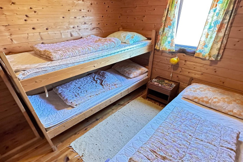 Værelse med køjeseng og enkeltseng i træhytte, lyse farver og vindue med blomstergardin i Danmark.