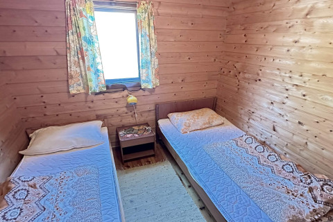Værelse med to enkeltsenge, trævægge, et vindue med farverige gardiner og et natbord i HUS 55762 HYTTE A i Danmark.