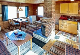 Hyggelig opholdsstue og køkken i HUS 55762 HYTTE A, Danmark, med trævægge og central pejs.