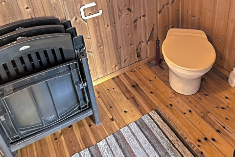 Billede af et træbeklædt toiletområde med plaststole, gulvtæppe og brunt toiletsæde i HUS 55762 HYTTE A.