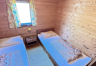 Et hyggeligt værelse på HUS 55762 HYTTE A i Danmark med to enkeltsenge, trævægge og farverige gardiner.