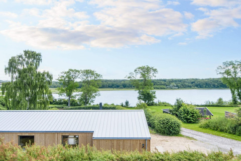 Casa de vacaciones de 4 estrellas en Rønde con vista al lago, árboles y naturaleza bajo cielo azul.